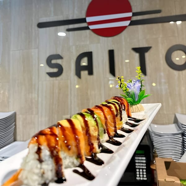 Saito Japanese Steakhouse's sushi roll with salmon, avocado, and eel sauce, with the restaurant logo in the background.