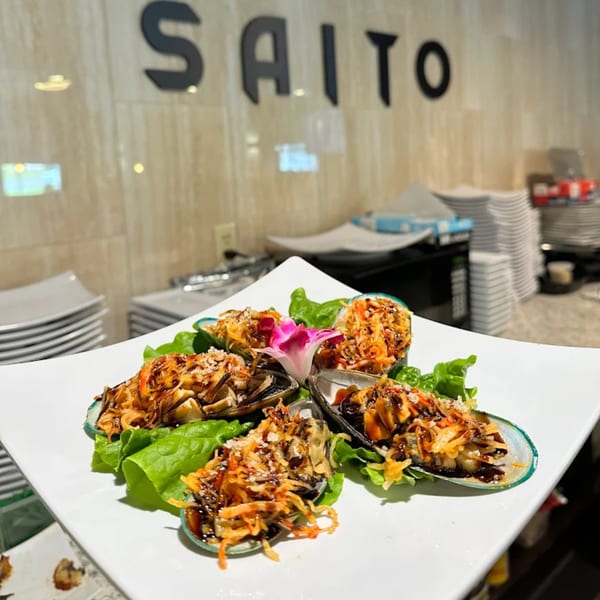 Saito Japanese Steakhouse's baked mussels, garnished with a pink flower, on a white plate.