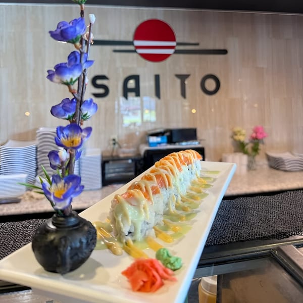 A long plate of Saito Japanese Steakhouse sushi rolls with sauces, ginger, and wasabi, with a floral decoration.
